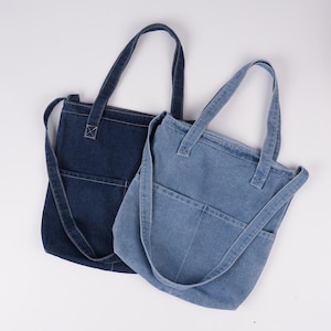 Peut inclure: Deux sacs fourre-tout en denim de diff&eacute;rentes nuances de bleu. L'un est indigo fonc&eacute;, l'autre plus clair. Chaque sac a une poche avant et de longues sangles pour &ecirc;tre port&eacute; &agrave; l'&eacute;paule. Les sacs sont en denim robuste.