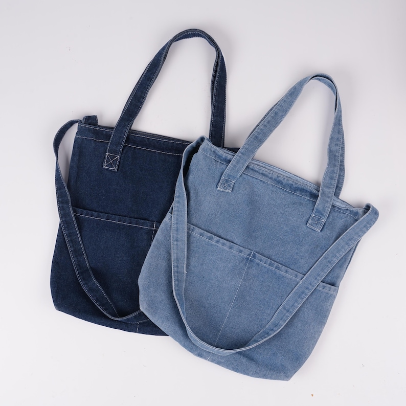 Peut inclure: Deux sacs fourre-tout en denim de diff&eacute;rentes nuances de bleu. L'un est indigo fonc&eacute;, l'autre plus clair. Chaque sac a une poche avant et de longues sangles pour &ecirc;tre port&eacute; &agrave; l'&eacute;paule. Les sacs sont en denim robuste.