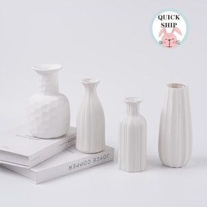 May include: A set of three ceramic mugs with a speckled, matte finish. The mugs are in shades of cream, light gray, and dark gray. Each mug has a simple, minimalist design and a rounded handle.