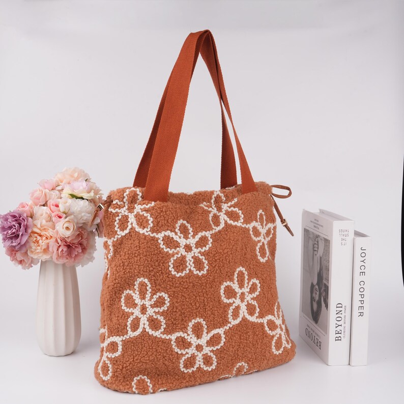 May include: A brown tote bag with white embroidered flowers. The bag has two brown straps and a drawstring closure.