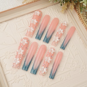May include: Set of ten pink and blue ombre press-on nails with white flower and rhinestone embellishments.