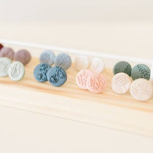May include: A wooden display shelf with a variety of small, round, colorful earrings. The earrings are made of clay and feature floral designs.