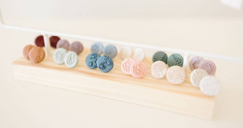 May include: A wooden display shelf with a variety of small, round, colorful earrings. The earrings are made of clay and feature floral designs.