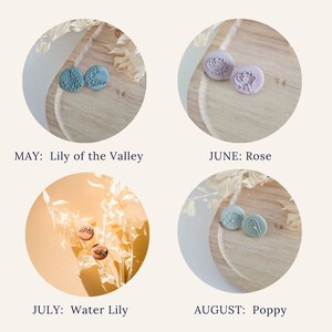 May include: Four pairs of small, round, clay earrings with different floral designs. The earrings are displayed on a wooden surface with a light brown background. The earrings are labeled with the months of May, June, July, and August, and the corresponding flower names: Lily of the Valley, Rose, Water Lily, and Poppy.
