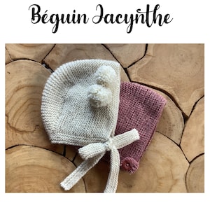 May include: Two knitted baby bonnets, one white with white pom-poms and one pink. The bonnets are on a wooden surface.