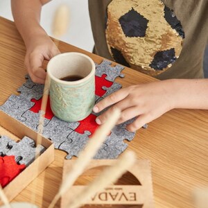 A focused shot of a child meticulously placing a red felt puzzle piece into a grey felt puzzle on a wooden table