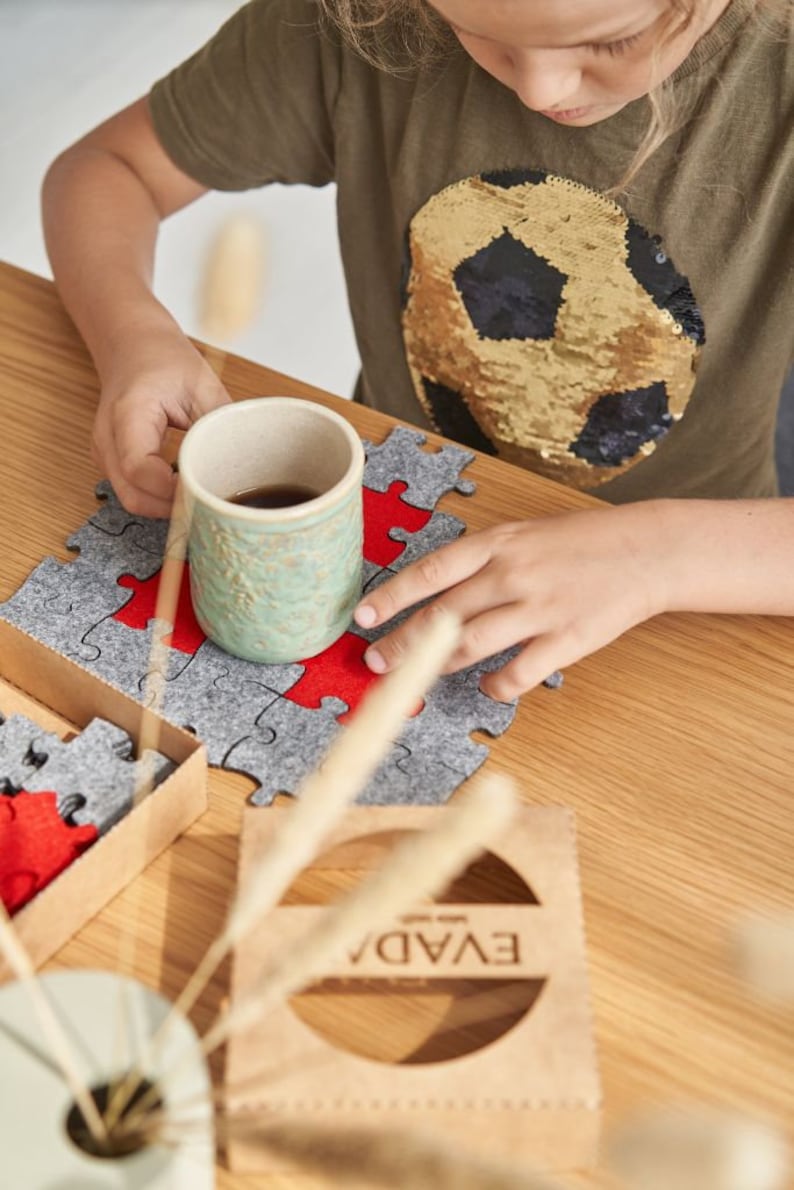 A focused shot of a child meticulously placing a red felt puzzle piece into a grey felt puzzle on a wooden table