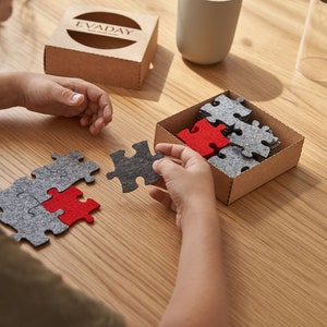 A child assembling grey and red felt puzzle pieces on a wooden table, with a box labeled "EVADAY" in the background.