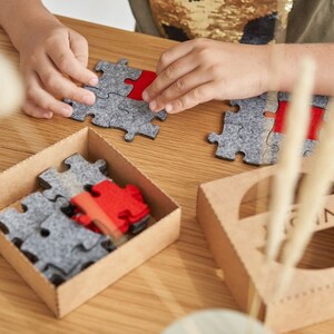 Overhead view of a child fitting grey and red felt puzzle pieces together on a wooden table.