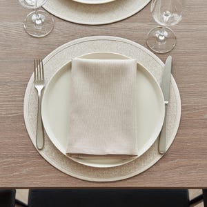 Op de afbeelding: Een beige placemat met een wit bord en een beige servet erop. Een zilveren vork en mes liggen rechts van het bord.