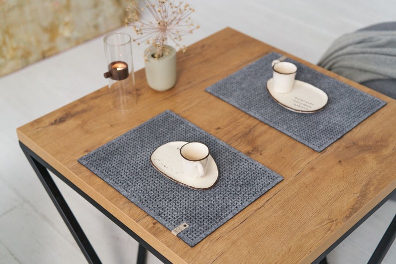 A neatly arranged wooden table with grey textured placemats, white ceramic plates, and small coffee cups, viewed from above.