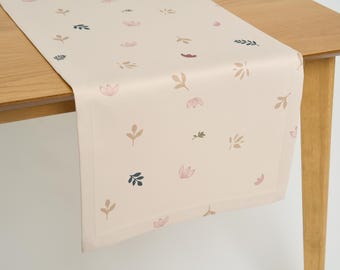 May include: A beige table runner with a delicate floral and leaf pattern in shades of pink, brown, and blue.
