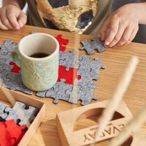 A child creating a pattern with grey and red felt puzzle pieces on a wooden table, accompanied by a mug and the "EVADAY" box.