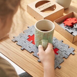 A child enjoying assembling grey and red felt puzzle pieces on a wooden table, with a mug in the background.