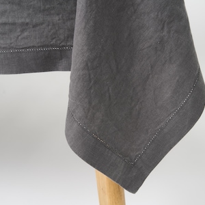 Puede incluir: Un mantel de lino gris oscuro con una textura sutil y un borde cosido.