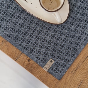 Close-up view of a wooden table corner with a grey textured placemat and a white ceramic plate.