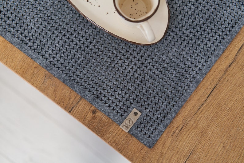 Close-up view of a wooden table corner with a grey textured placemat and a white ceramic plate.