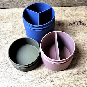 May include: Three cylindrical containers in shades of blue, green, and purple. The blue container is divided into three sections. The purple and green containers are divided into two sections. All containers are on a wooden surface.