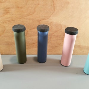 May include: Five cylindrical containers with black lids. The containers are in different colors: beige, green, blue, pink, and light blue.