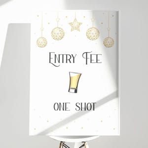 以下が含まれることがあります： 「Entry Fee」と「One Shot」の文字と金色のアクセントが入った白いサイン。中央には、黄色の液体が入ったショットグラスのイラスト。上部には金色の星と球体の装飾が吊り下げられています。