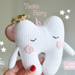 Puede incluir: Una hada de los dientes de crochet blanco con alas rosas, halo dorado y ojos cerrados. El hada de los dientes está sosteniendo una flor rosa. El texto "Tooth Fairy" está escrito encima del hada de los dientes. El texto "by *gabi*SPONGE*" está escrito debajo del hada de los dientes. El texto "DIGITAL PATTERN (pdf)" está escrito en un cuadro rosa en la esquina inferior derecha de la imagen.
