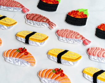 Puede incluir: Una colección de 14 parches de sushi bordados, que representan diferentes tipos de sushi, incluyendo nigiri, maki y sashimi. Los parches están hechos con hilo de colores y tienen un fondo blanco.