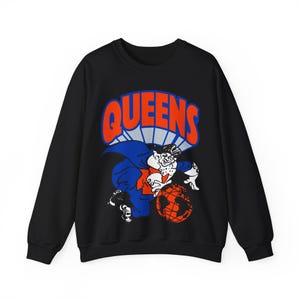 May include: Black sweatshirt with a graphic print of a cartoon character holding a globe. The text "QUEENS" is printed in red and white above the character.
