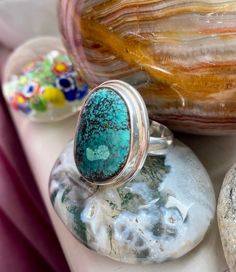 May include: A silver ring with a turquoise stone set in a bezel setting. The stone has a green and blue color with a marbled pattern.