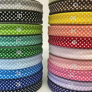 Könnte beinhalten: Stapel von Polka-Dot-Bändern in verschiedenen Farben, darunter Schwarz, Weiß, Grün und Blau. Jede Bandrolle ist mit einer Nummer versehen. Die Bänder eignen sich für Bastelarbeiten, Geschenkverpackungen oder Dekorationszwecke.