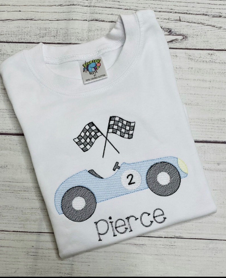Peut inclure: T-shirt blanc avec une voiture de course bleu clair, le num&eacute;ro 2, et deux drapeaux &agrave; damier. Le nom "Pierce" est brod&eacute; en noir. Le t-shirt a un col rond et une petite &eacute;tiquette.