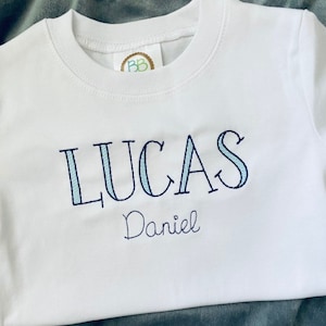 May include: White t-shirt with blue and white striped lettering that says "LUCAS Daniel"