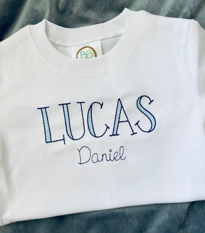 May include: White t-shirt with blue and white striped lettering that says "LUCAS Daniel"