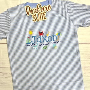 May include: A light blue and white striped t-shirt with the name "Jaxon" embroidered in blue, along with beach-themed designs like a sailboat, sun, crab, and waves. The shirt also has the text "DinoSew SUITE" on a tag.