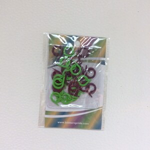 May include: A clear plastic bag containing green and burgundy plastic stitch markers. The bag has a white label with the text "www.knitterspride.com".