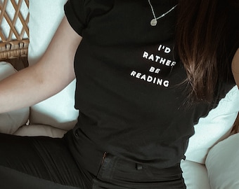 May include: A black t-shirt with the text "I'd rather be reading" in white lettering. The person is wearing black jeans and black boots.