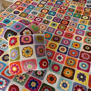 Könnte beinhalten: Eine farbenfrohe, handgehäkelte Decke und zwei passende Kissen. Die Decke und die Kissen weisen ein Patchwork-Design mit floralen Motiven in verschiedenen Farben auf, darunter Rot, Gelb, Blau und Grün. Die Decke liegt auf einem Bett.