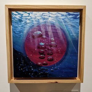 May include: A framed painting of a red orb with bubbles rising from it, surrounded by blue water and light rays. The painting has a dark blue and black background.