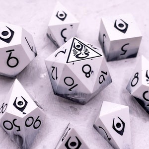 Op de afbeelding: Een set van acht witte en zwarte dobbelstenen met een uniek oogsymbool op elke zijde. De dobbelstenen zijn gemaakt van een gemarmerd materiaal met een zwart-wit swirl-patroon.