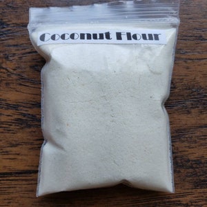 Peut inclure: Un sac en plastique transparent rempli de farine de coco blanche. Le sac porte une &eacute;tiquette blanche sur laquelle est inscrit "Coconut Flour".