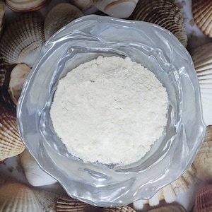 Peut inclure: Une poudre blanche dans un bol en verre transparent &agrave; bord festonn&eacute;. Le bol est entour&eacute; de coquillages.