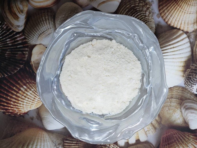 Peut inclure: Une poudre blanche dans un bol en verre transparent &agrave; bord festonn&eacute;. Le bol est entour&eacute; de coquillages.