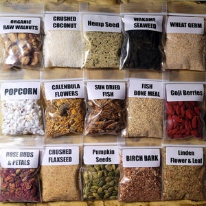 Puede incluir: Una variedad de ingredientes secos en bolsas de plástico transparente, incluyendo nueces, coco, semillas de cáñamo, algas marinas y germen de trigo. Otras bolsas contienen palomitas de maíz, flores de caléndula, pescado seco al sol, harina de huesos de pescado y bayas de goji. Bolsas adicionales contienen capullos de rosa, linaza, semillas de calabaza, corteza de abedul y flor y hoja de tilo.