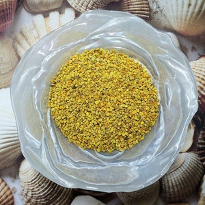 May include: A clear glass bowl filled with a large amount of yellow bee pollen granules.