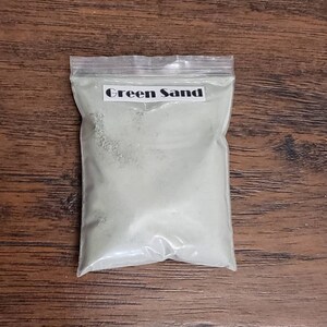 May include: A clear plastic bag filled with green sand. The bag has a label that says "Green Sand".