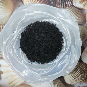 Puede incluir: Un peque&ntilde;o taz&oacute;n blanco con polvo negro en su interior. El taz&oacute;n est&aacute; sobre una superficie con conchas marinas.