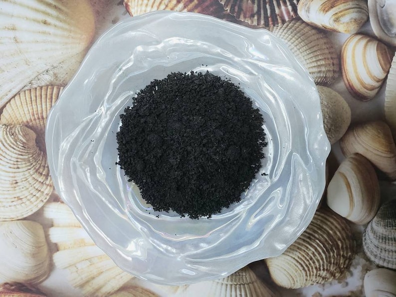 Puede incluir: Un peque&ntilde;o taz&oacute;n blanco con polvo negro en su interior. El taz&oacute;n est&aacute; sobre una superficie con conchas marinas.
