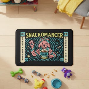 A rectangular pet feeding mat featuring a retro mystical graphic titled SNACKOMANCER in beige arched text. The center illustration depicts a pink dog wearing a teal turban, waving one paw and gazing into a crystal ball that is actually a bowl of food labeled MORE. The background is black with teal wavy lines and floating fish bones. Side panels in beige and teal feature paw prints and text reading TREAT PROPHECY and DINNER DIVINATION. The mat is made of neoprene with a non-slip backing.