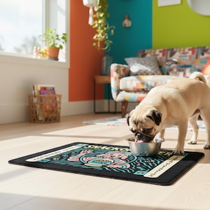 A rectangular pet feeding mat featuring a retro mystical graphic titled SNACKOMANCER in beige arched text. The center illustration depicts a pink dog wearing a teal turban, waving one paw and gazing into a crystal ball that is actually a bowl of food labeled MORE. The background is black with teal wavy lines and floating fish bones. Side panels in beige and teal feature paw prints and text reading TREAT PROPHECY and DINNER DIVINATION. The mat is made of neoprene with a non-slip backing.