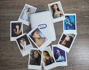 May include: A white instant camera with a variety of printed photos surrounding it. The photos feature different people and scenes. The camera has the word "instax" printed on it.