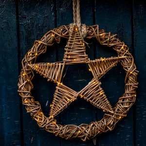 May include: A woven wicker star with warm white fairy lights, hanging against a dark blue wooden background.